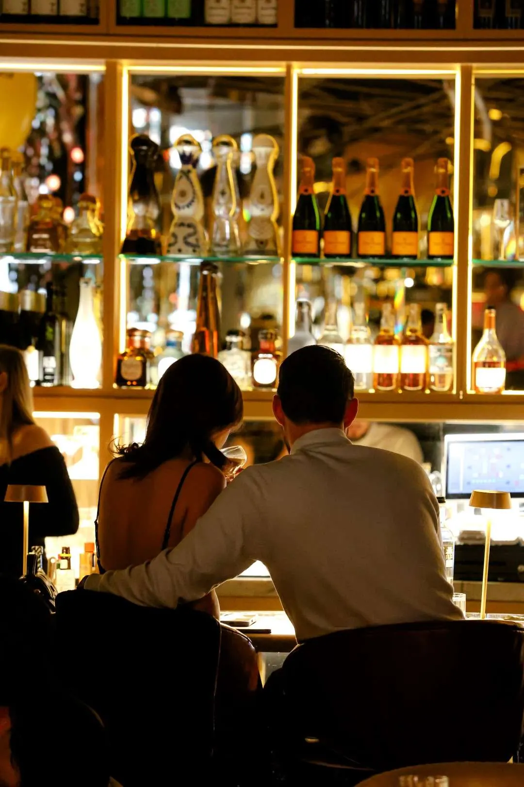 Couple at the bar in front of the champagne wall