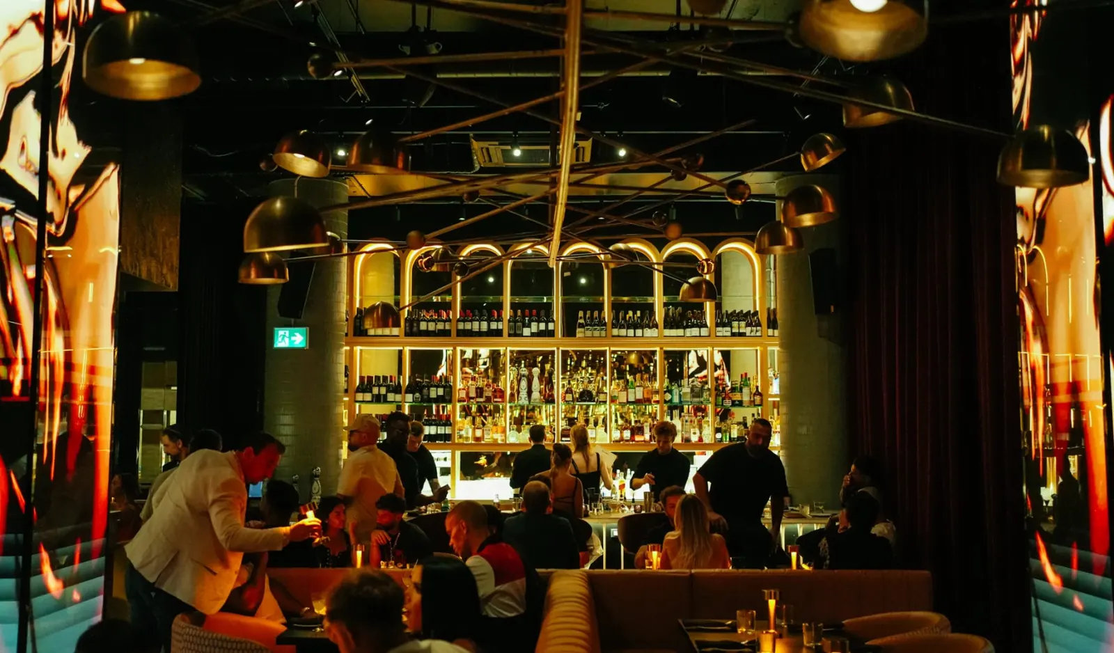 A full house beneath brass pendant lamps and the gold-lit arched bar at Maxime’s