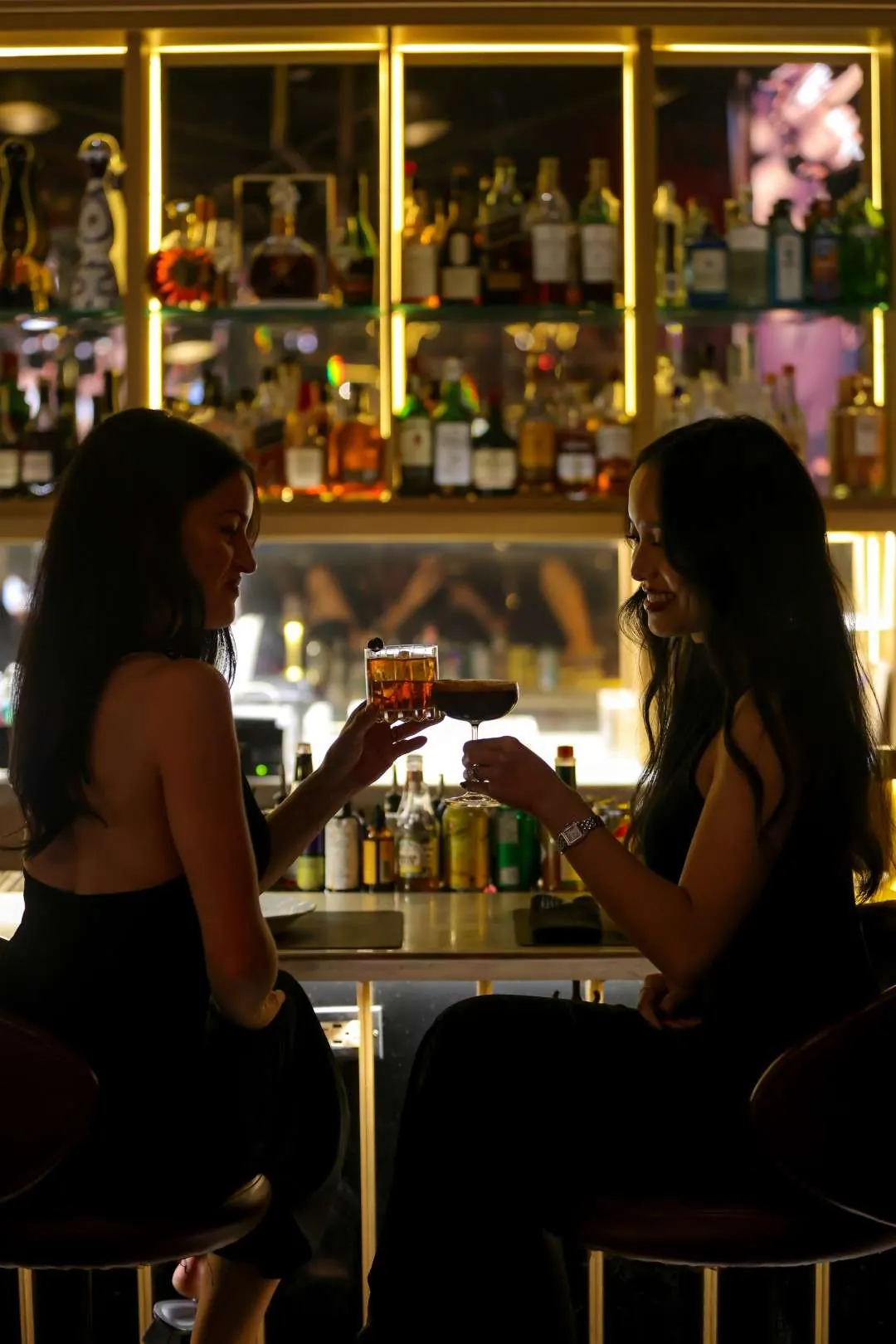 Two guests toasting with cocktails at the gold-lit backlit bar