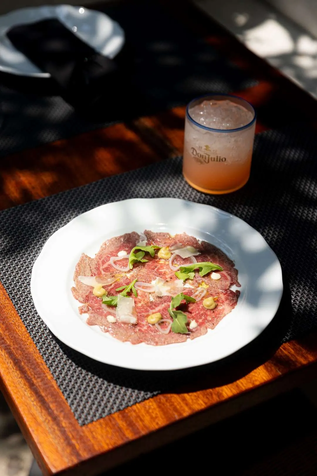 Thinly sliced beef with herbs and parmesan on a dark wood table