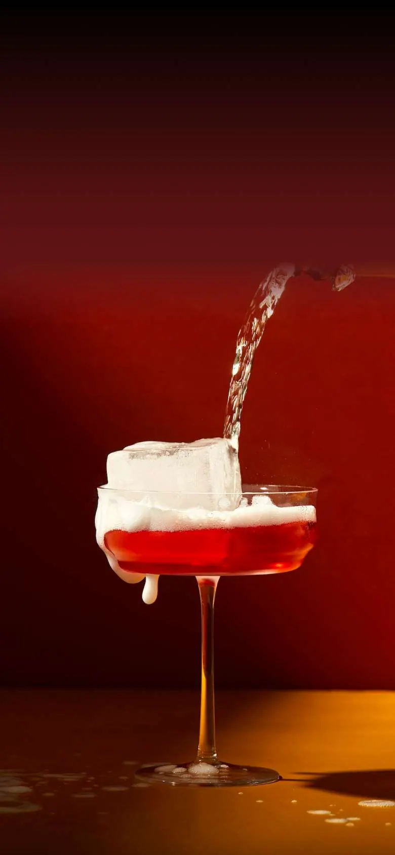 Red foam-topped cocktail being poured in the dark