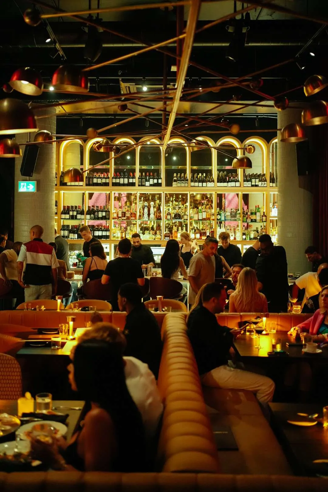Full dining room with leather banquettes facing the bar