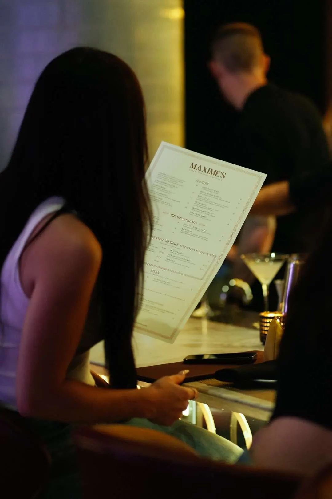 A guest reading the Maxime’s menu at the bar