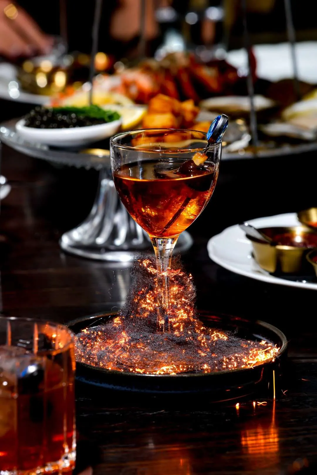 A cocktail over a bed of sparkling embers beside the seafood tower
